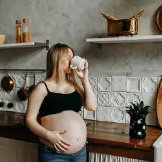 Kobieta w zaawansowanej ciąży pije napój z kubka w kuchni. Czkawka w ciąży to częste zjawisko.