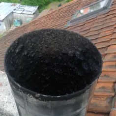 Zatkany komin pokryty smołą, jakby ktoś wylał na niego płynną folię. Ciemna masa blokuje przepływ powietrza, powodując nieprzyjemny zapach.