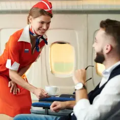 Uśmiechnięta stewardessa w czerwonym stroju podaje kawę pasażerowi w samolocie.