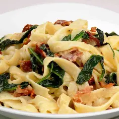 Makaron tagliatelle z sosem śmietanowym, szpinakiem i kawałkami boczku.