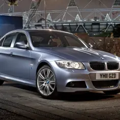 Srebrny sedan BMW E90 330d stoi na ulicy nocą, z tyłu widać stadion.
