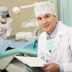 Dentysta z uśmiechem trzyma dokumentację, podczas gdy asystentka bada małą pacjentkę. Czy 5 to mleczak?