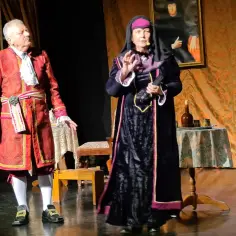 Dwoje aktorów w strojach historycznych na scenie teatralnej.