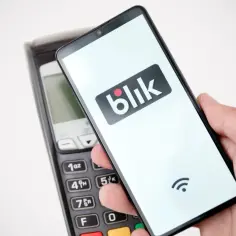 Dłoń trzyma smartfon z logo Blik nad terminalem płatniczym. Czyżby awaria Blik uniemożliwiła płatność?