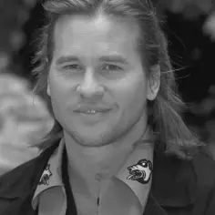 Val Kilmer, znany z wielu filmów, uśmiecha się do obiektywu. Jego charakterystyczna koszula z nadrukiem dodaje mu uroku.