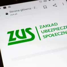 Telefon z logo ZUS na ekranie, otoczony monetami. Marzenie o wakacjach od ZUS 2026 staje się bliższe.