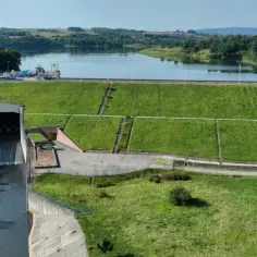 Zapora z budynkami i infrastrukturą, część większego kompleksu elektrowni wodnych. Woda spływa do kanału.