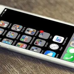 Biały iPhone z widokiem ekranu głównego z ikonami aplikacji i paskiem Dock.