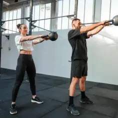 Kobieta i mężczyzna wykonują ćwiczenia z kettlebellami w siłowni.