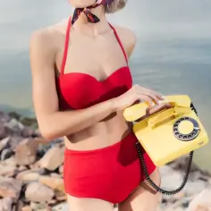 Kobieta w czerwonym bikini trzyma żółtą słuchawkę telefonu. Co to bikini?