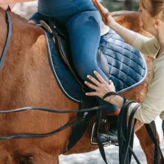 Instruktorka pomaga jeźdźcowi na koniu. Zastanawiasz się, ile kosztuje odznaka jeździecka?