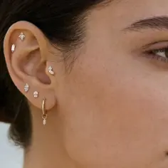 Ucho ozdobione kilkoma błyszczącymi kolczykami do piercingu ucha, w tym krzyżykiem i wiszącym elementem.