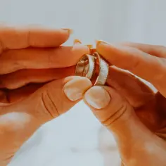 Dwie dłonie trzymają obrączki. Jedna z nich, z widoczną na palcu obrączką, symbolizuje, kto nosi obraczkę na lewej dloni.