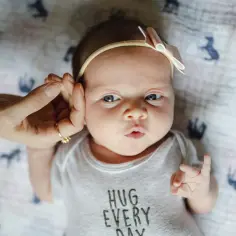 Uroczy 3 tygodniowy noworodek w body z napisem "HUG EVERY DAY", z delikatną opaską na głowie.
