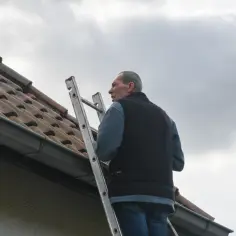 Mężczyzna na drabinie przy dachu. Jak obliczyć kąt nachylenia dachu jednospadowego?