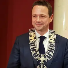 Uśmiechnięty prezydent Warszawy w garniturze i łańcuchu z godłem miasta.