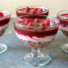 Pyszny deser z mascarpone i galaretką malinową w pucharkach, ozdobiony świeżymi malinami.