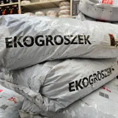 Stos worków z ekogroszkiem, widoczne napisy "EKOGROSZEK" i logo "Popularny".