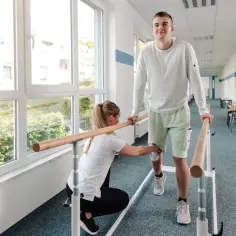 Fizjoterapeutka pomaga pacjentowi przy poręczy. Dowiedz się, jak uzyskać świadczenie rehabilitacyjne po ustaniu zatrudnienia.