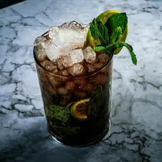 Orzeźwiający drink z jagermeister, lodem, miętą i limonką na marmurowym blacie. Idealny na letnie wieczory.