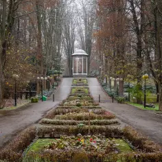 Alejka w parku, gdzie leży Polanica Zdrój, prowadzi do altany. Jesienne drzewa i klomby tworzą malowniczy widok.