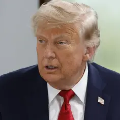 Donald Trump w garniturze i czerwonym krawacie, z amerykańską flagą na klapie, szuka porozumienia.
