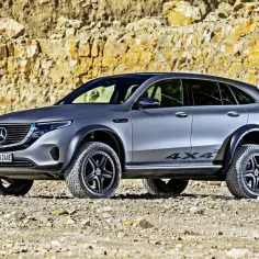 Szary Mercedes 4x4 z terenowymi oponami i felgami stoi na kamienistym podłożu, na tle skalnej ściany.