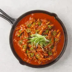 Kurczak w sosie gochujang, podany w żeliwnej patelni, ozdobiony zieloną cebulką i sezamem.