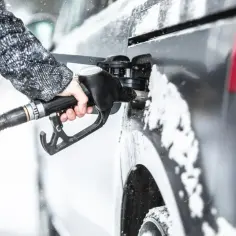 Dłoń trzymająca pistolet paliwowy przy samochodzie pokrytym śniegiem.