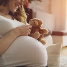 Uśmiechnięta ciężarna kobieta trzyma misia na brzuchu. Kiedy najpóźniej zaczyna bić serce płodu?
