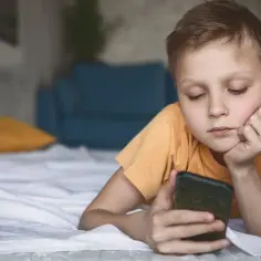 Chłopiec leży na łóżku z telefonem, zastanawiając się, czy dziecko może usunąć Family Link.