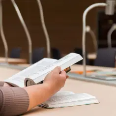 Osoba studiuje, szukając odpowiedzi na problem badawczy. Przykładem jest skupienie na tekście w bibliotece.