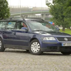 Ciemnoniebieski Volkswagen Passat kombi, model b5, stoi na brukowanym placu.