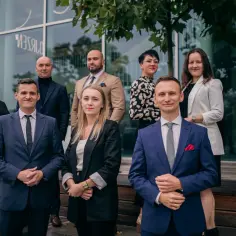 Grupa prawników w eleganckich strojach stoi przed nowoczesnym budynkiem.