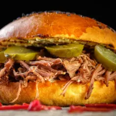 Soczysta maczanka krakowska z szarpaną wieprzowiną, ogórkiem kiszonym i pikantnymi papryczkami. Pyszny, sycący burger.