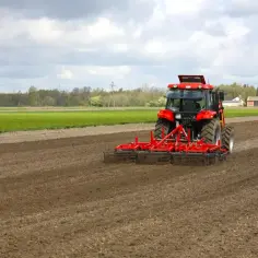 Czerwony traktor z agregatem uprawowym na polu. Przygotowanie gleby pod zasiew, jak wniosek o przedłużenie umowy dzierżawy kowr wzór.