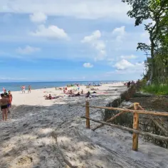 Słoneczny dzień na plaży w Karwieńskich Błotach Drugich. Ludzie odpoczywają na piasku, dzieci bawią się blisko morza.