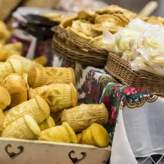 Oscypek w drewnianej skrzynce i plecionej koszyczku, obok ser w plastiku.