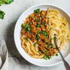 Porcja spaghetti z sosem z soczewicy i warzyw, posypana natką pietruszki.