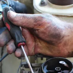 Brudna ręka mechanika przykręca śrubę, kontynuując wymianę linki sprzęgła w samochodzie.