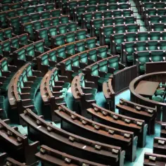Puste zielone fotele w sali sejmowej z drewnianymi ławami i mównicą.