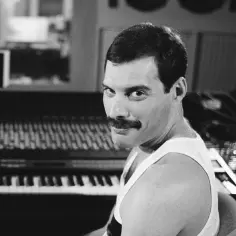 Freddie Mercury z wąsami i w białej koszulce, siedzi przy pianinie. Czy Freddie Mercury miał dzieci? Nie, nie miał.