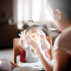Opiekunka karmi dziecko, które trzyma zabawkę. Zastanawiasz się, ile kosztuje opiekunka do dziecka?