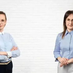 Dwie kobiety w koszulach na tle białej ceglanej ściany.