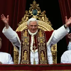 Papież Benedykt XVI z podniesionymi rękami błogosławi świat, urbi et orbi. Obok niego dwaj duchowni.