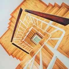 Drewniane schody zabiegowe z białymi poręczami i ciemnymi drewnianymi uchwytami, widziane z góry, tworzą spiralny wzór.