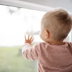 Dziecko w paski patrzy przez okno, dotykając szyby.