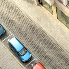 Zastanawiasz się, ile kosztuje miejsce parkingowe pod blokiem? Na zdjęciu widać rząd samochodów zaparkowanych na brukowanej ulicy, obok kamienicy.