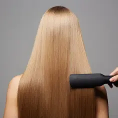 Prostowanie włosów prostownicą, efekt bioplastia. Długie, blond włosy stają się idealnie gładkie i lśniące.