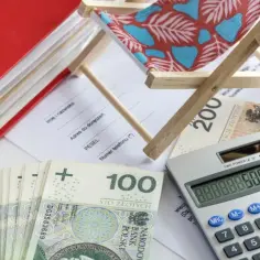 Kalkulator, pieniądze i miniaturowa leżanka sugerują planowanie wakacji i świadczenie urlopowe.